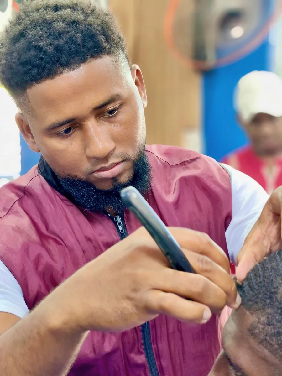 A focused barber uses a razor to shape a client's hairline in a modern barbershop.