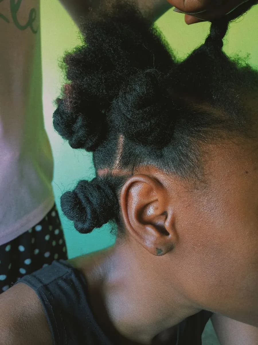 Detailed view of a young child getting bantu knots styled in a bright indoor setting.